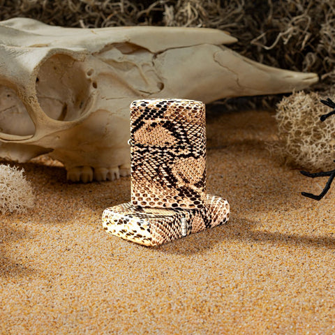 Lifestyle image of two Snake Skin 540 Color Windproof Lighter, one showing the front and standing on the other. The lighters are in a western theme, with sand, a bull skull, and tumbleweed.