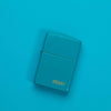 Lifestyle image of Classic Flat Turquoise Zippo Logo Windproof Lighter laying on a turquoise surface