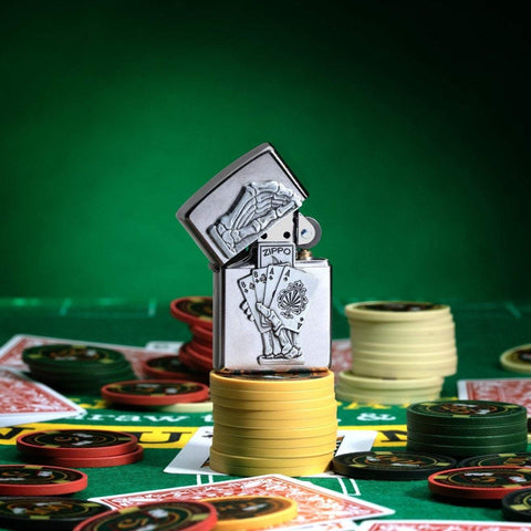 Dead Mans Hand Surprise Emblem Design Street Chrome™ Windproof Lighter standing on stacked poker chips, with cards and chips scattered all around a poker table.