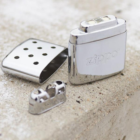 Lifestyle image of 12-Hour High Polish Chrome Refillable Hand Warmer, with its lid and burner laying on the ground next to it