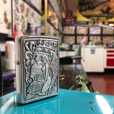 Lifestyle image of Skull and Angel Emblem Design Street Chrome™ Windproof Lighter standing within a tattoo parlor with art on the walls.