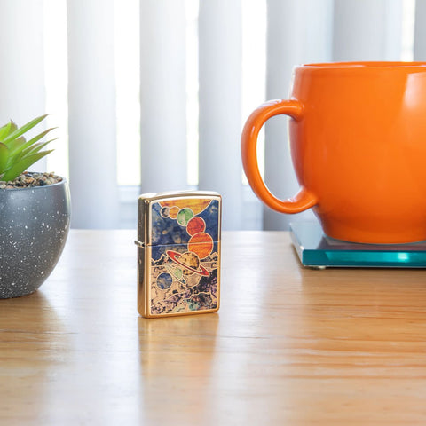 Lifestyle image of Fusion Space High Polish Brass Windproof Lighter, standing on an end stand with a plant and a coffee mug