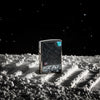 Front view of the High Polish Chrome Moon Landing Design Lighter shot with a galaxy background, sitting in gray sand 
