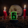 Lifestyle image of UFO Design Glow In The Dark Windproof Lighter glowing with a skull and candles behind it.