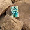 Lifestyle image of Lion Design Flat Sand Windproof Lighter laying on rocks.