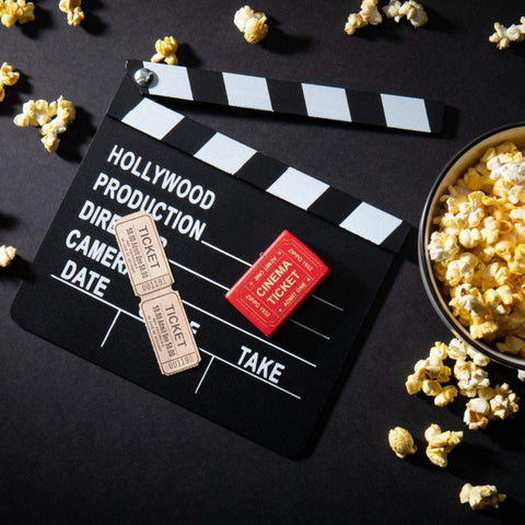 Lifestyle image of Cinema Ticket Red Matte Windproof Lighter laying on a movie clapperboard with popcorn scattered around it