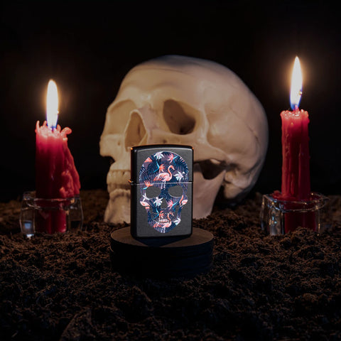 Lifestyle image of Flamingo Skull Design Black Matte Windproof Lighter with a skull and candles in the background.