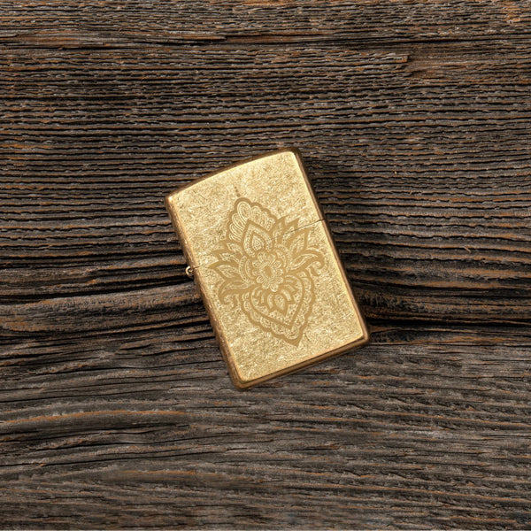 Lifestyle image of Henna Tattoo Design Tumbled Brass Windproof Lighter laying flat on a wooden table.