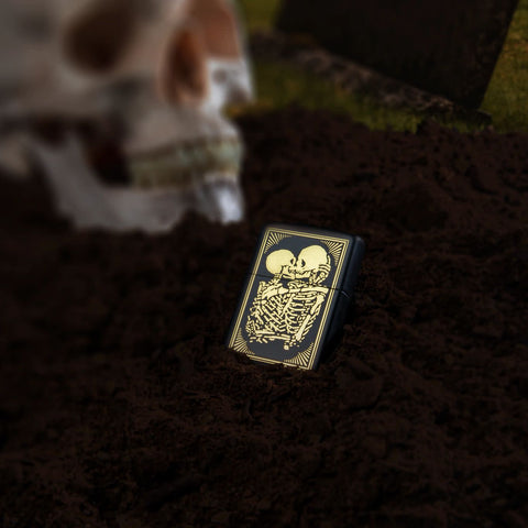 Lifestyle image of Lovers Design Black Matte Windproof Lighter laying in the dirt with a skull behind it.